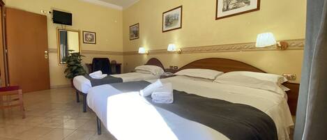 Une chambre d’hôtel avec deux lits, un bureau, une chaise, une télévision et des tableaux encadrés au mur.