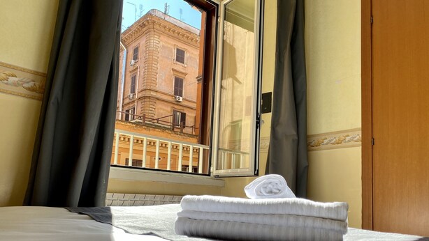 A hotel room with a bed, a window with curtains, and a view of a building outside.