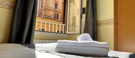 Quarto de hotel com cama, janela com cortinas e vista para um prédio.