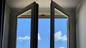 A room with a large window, a door, and a view of buildings outside.