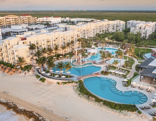 A resort with multiple buildings, a central swimming pool, and a beach area.