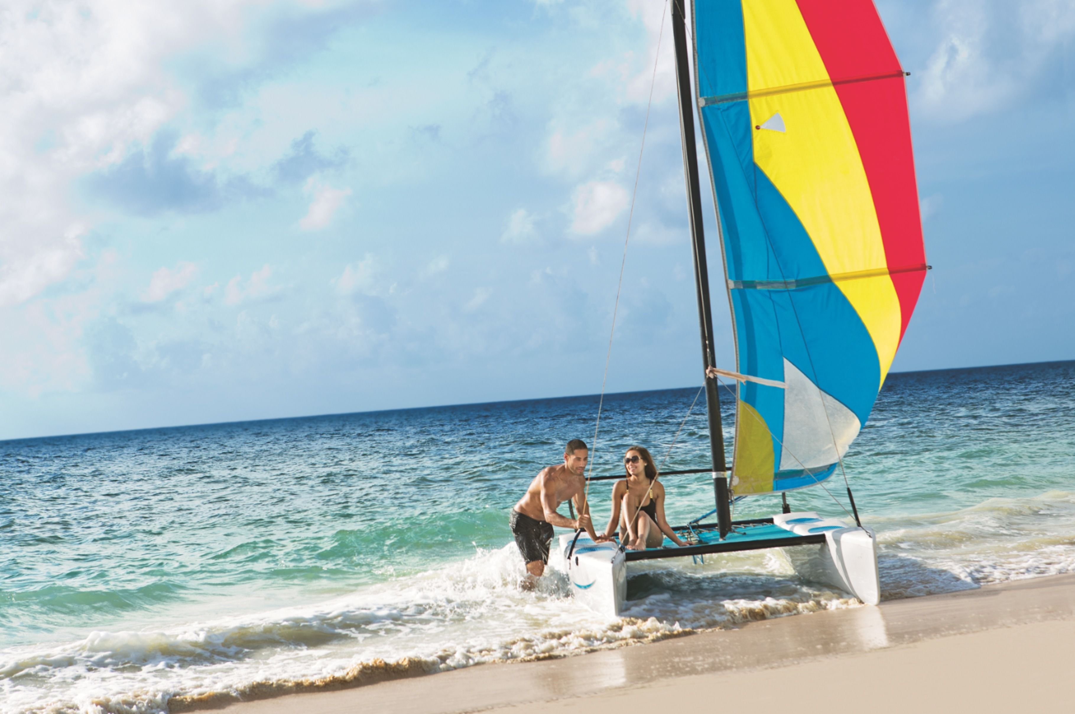 A sailboat with a colorful sail on a beach.