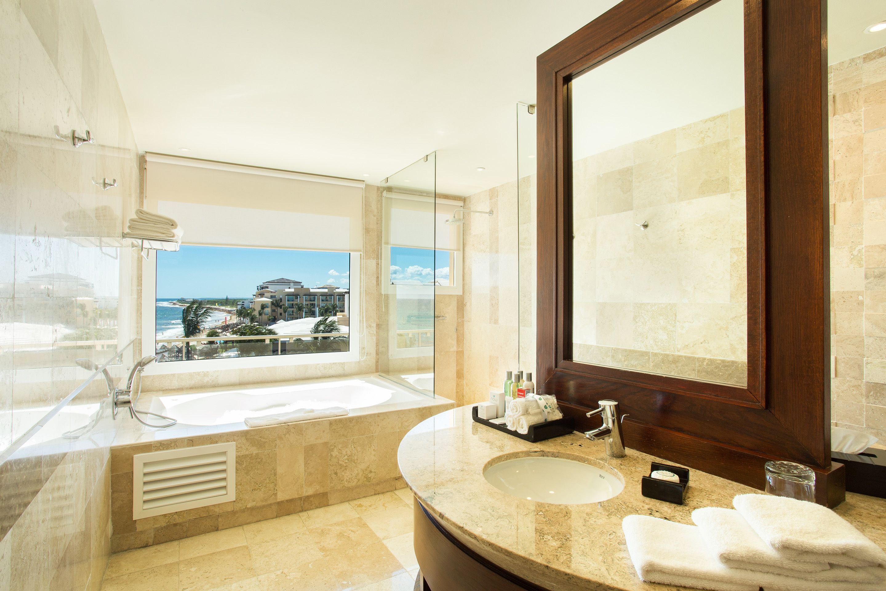 A modern bathroom with a large bathtub, a sink, and a mirror. There is a window providing a view of the ocean.