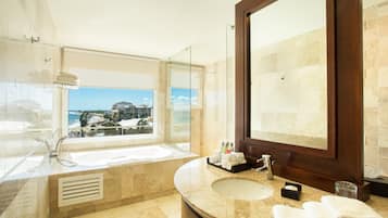 A modern bathroom with a large bathtub, a sink, and a mirror. There is a window providing a view of the ocean.