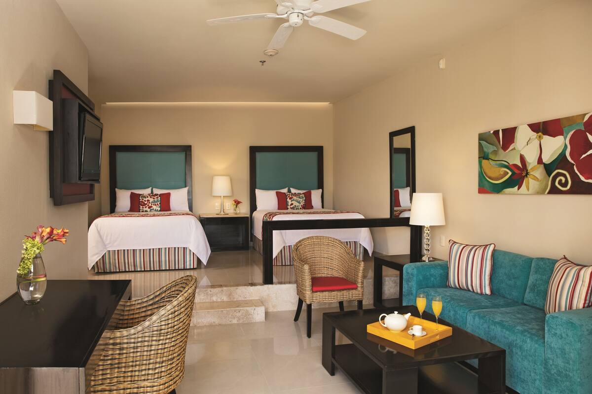 A hotel room with two beds, a sofa, a coffee table, and a TV.