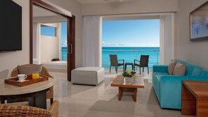 A modern living room with a large window overlooking the sea, a ceiling fan, and a dining area with a tray of orange juice. - Dreams Jade Resort & Spa - All Inclusive (Puerto Morelos)