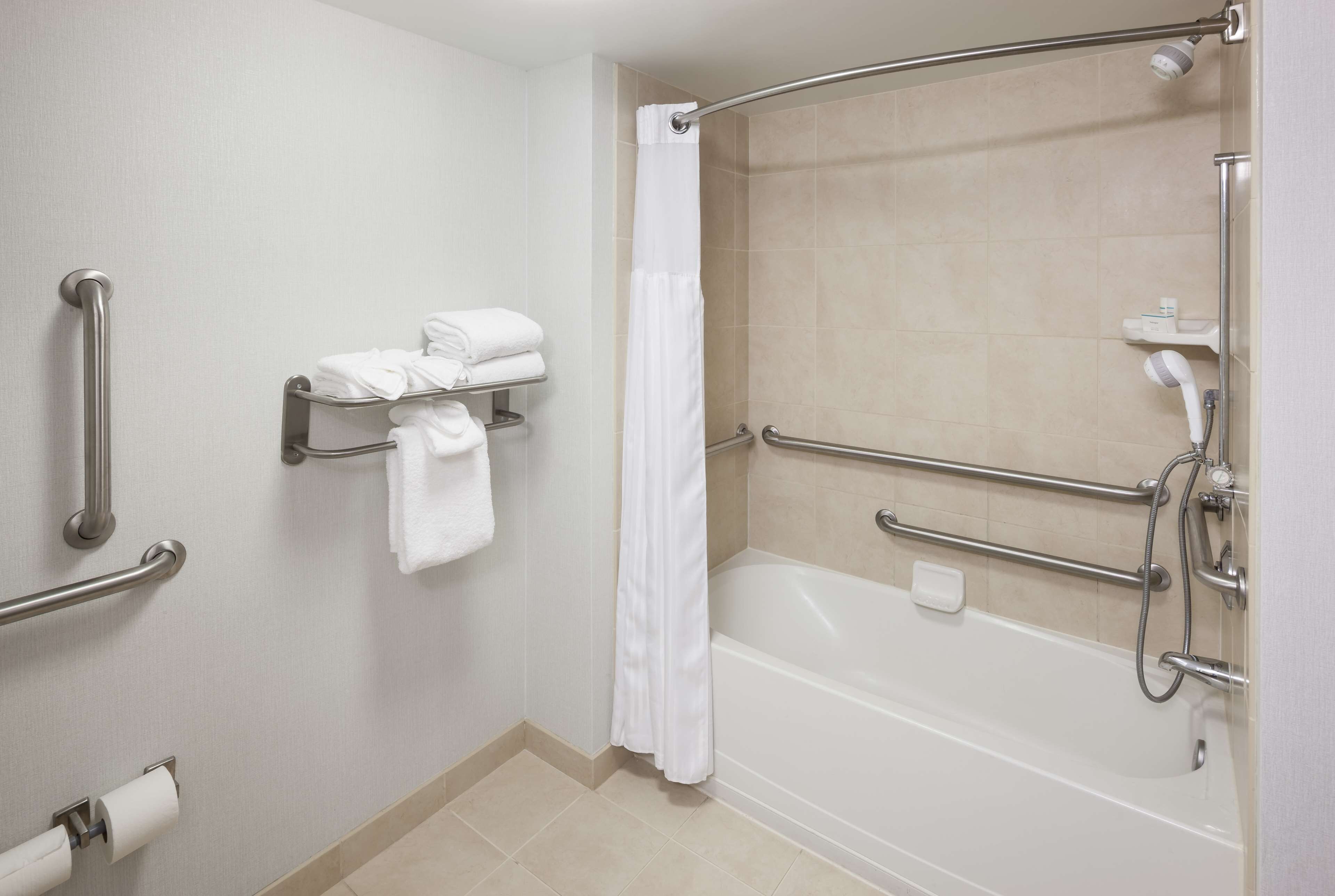 Une salle de bain équipée d’une baignoire, de barres d’appui, d’un porte-serviettes et d’un rideau de douche.