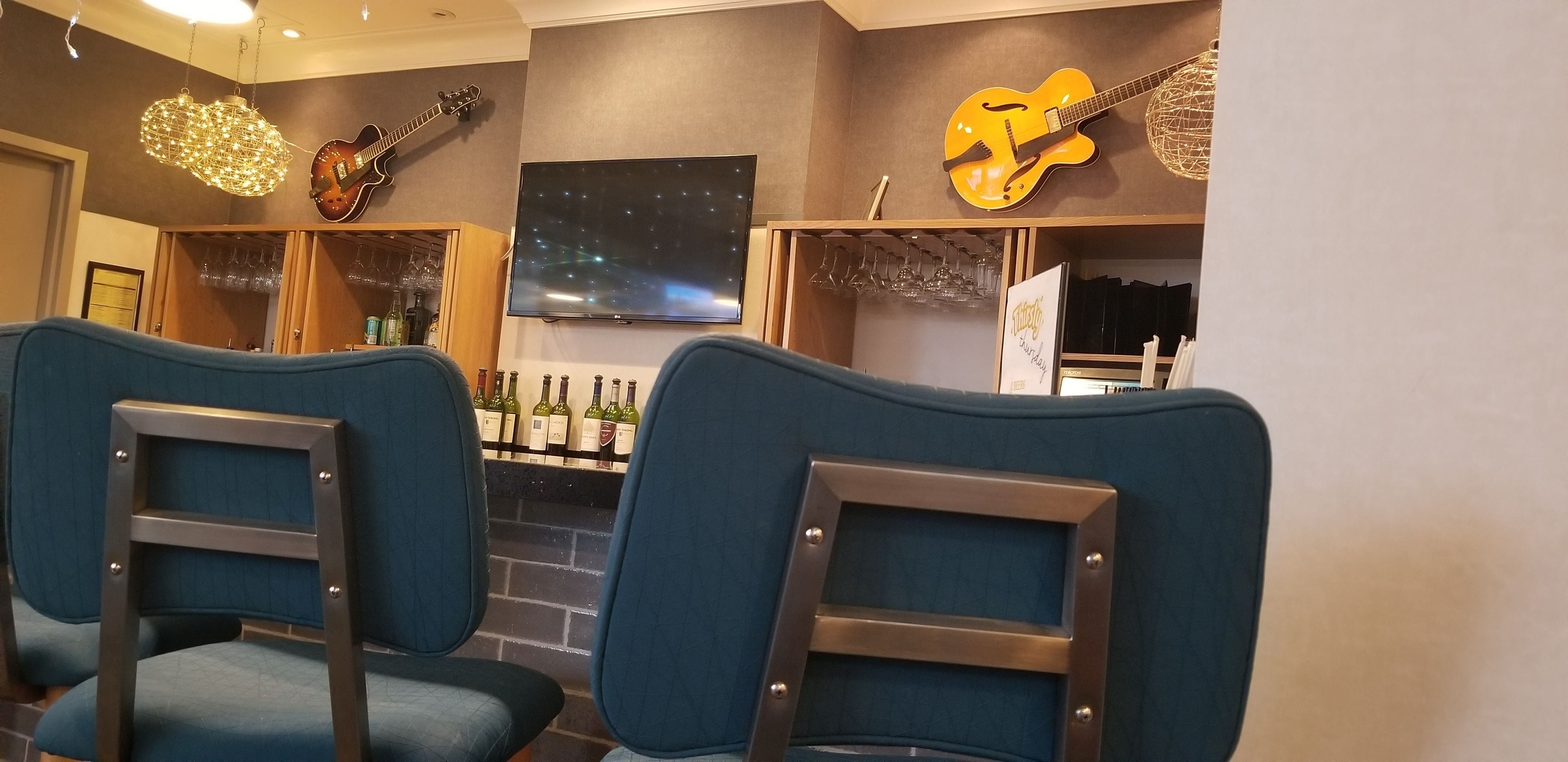 A bar area with blue cushioned chairs, a flat-screen TV, and guitars on the wall.