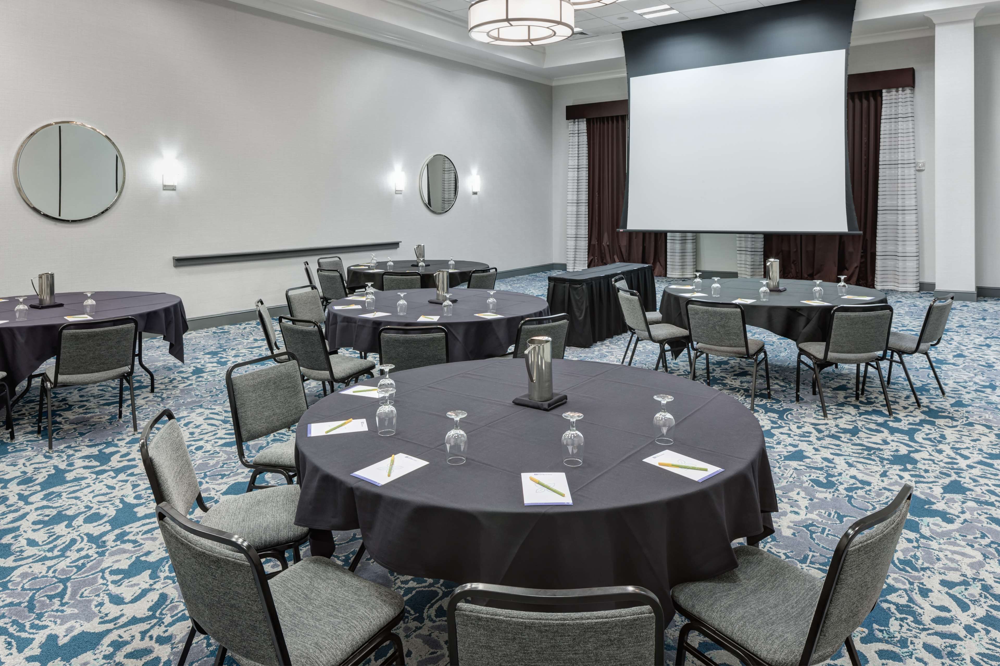 Une salle de conférence équipée de tables rondes, de chaises et d’un écran de projection.