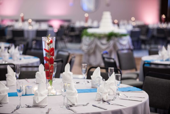 A banquet hall with round tables set for a formal event, featuring white tablecloths, folded napkins, and clear glassware.