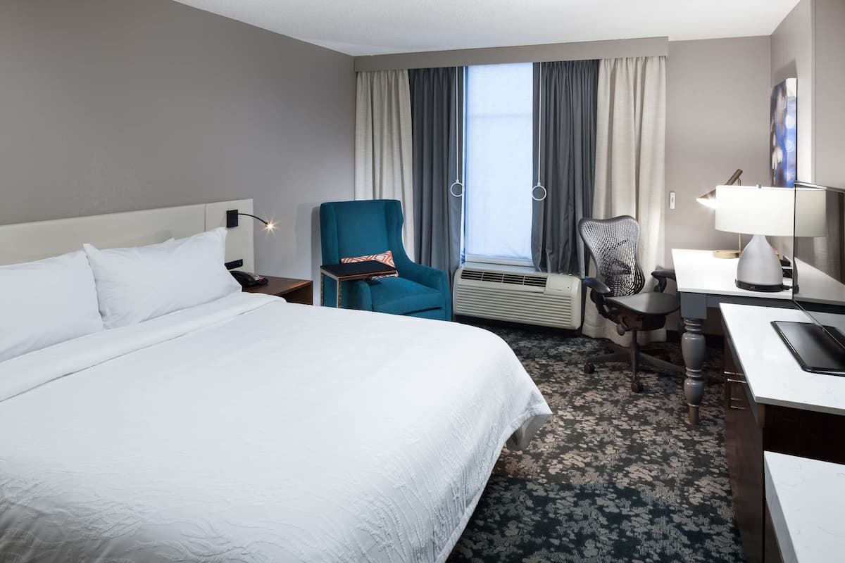 Ein Hotelzimmer mit einem großen Bett, einem Schreibtisch mit Lampe, einem Sessel und einer zusätzlichen Schreibtischlampe.