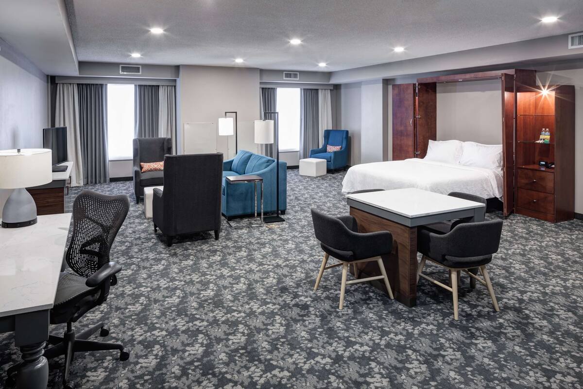 Ein Hotelzimmer mit Bett, Schreibtisch mit Stuhl, Sofa, Fernseher und Kleiderschrank.