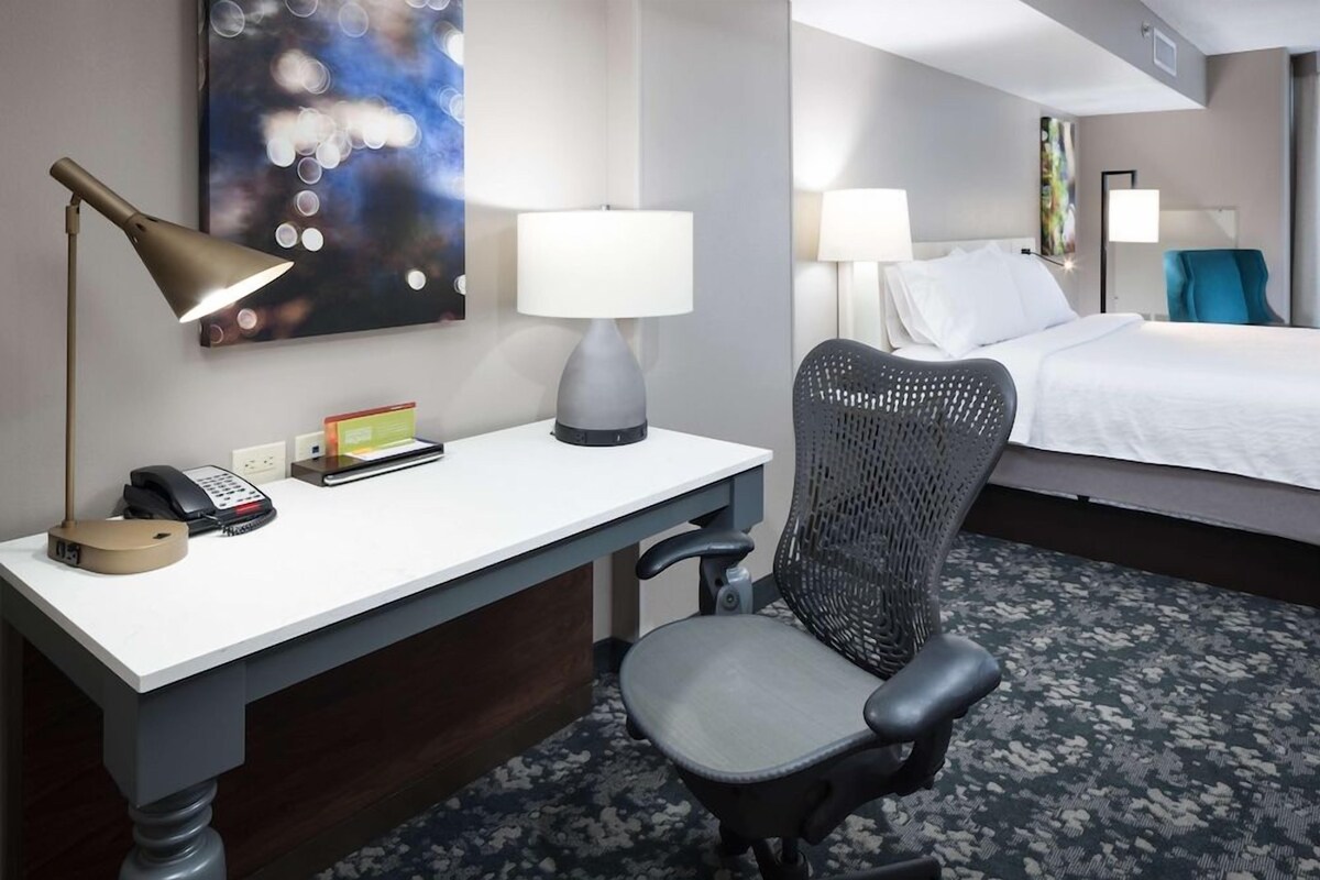 Ein Hotelzimmer mit Schreibtisch, Stuhl, Bett und einem Kunstwerk an der Wand.
