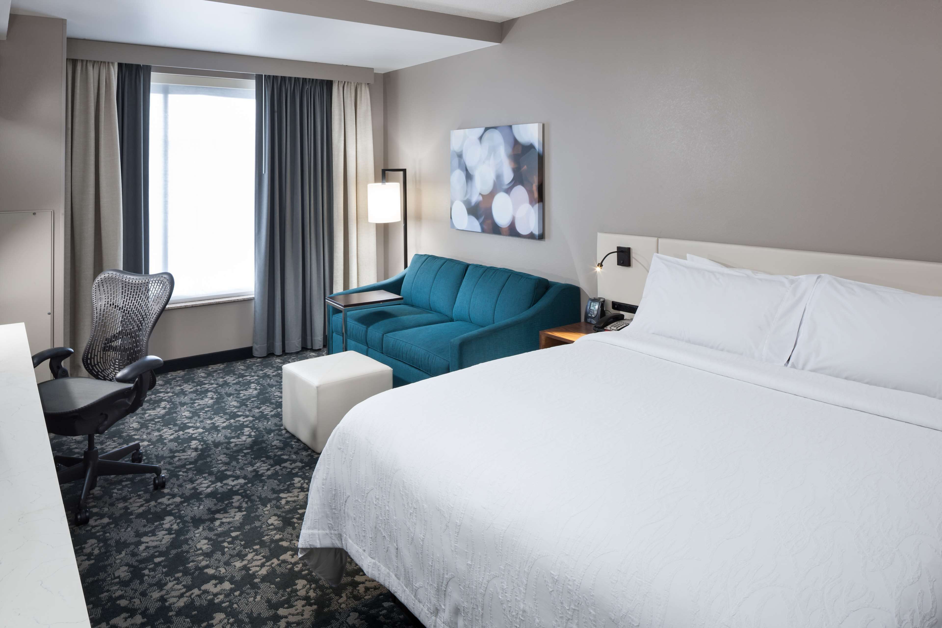 Una habitación de hotel con una cama grande, un sofá azul, un escritorio con una silla y una ventana con cortinas.