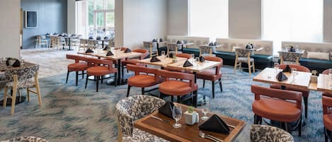 Un restaurante amplio con varias áreas de comedor, incluyendo cabinas y mesas, y ventanas grandes que ofrecen luz natural.