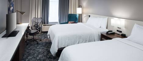 A hotel room with two beds, a desk with a computer, a chair, a TV, and a window with curtains.