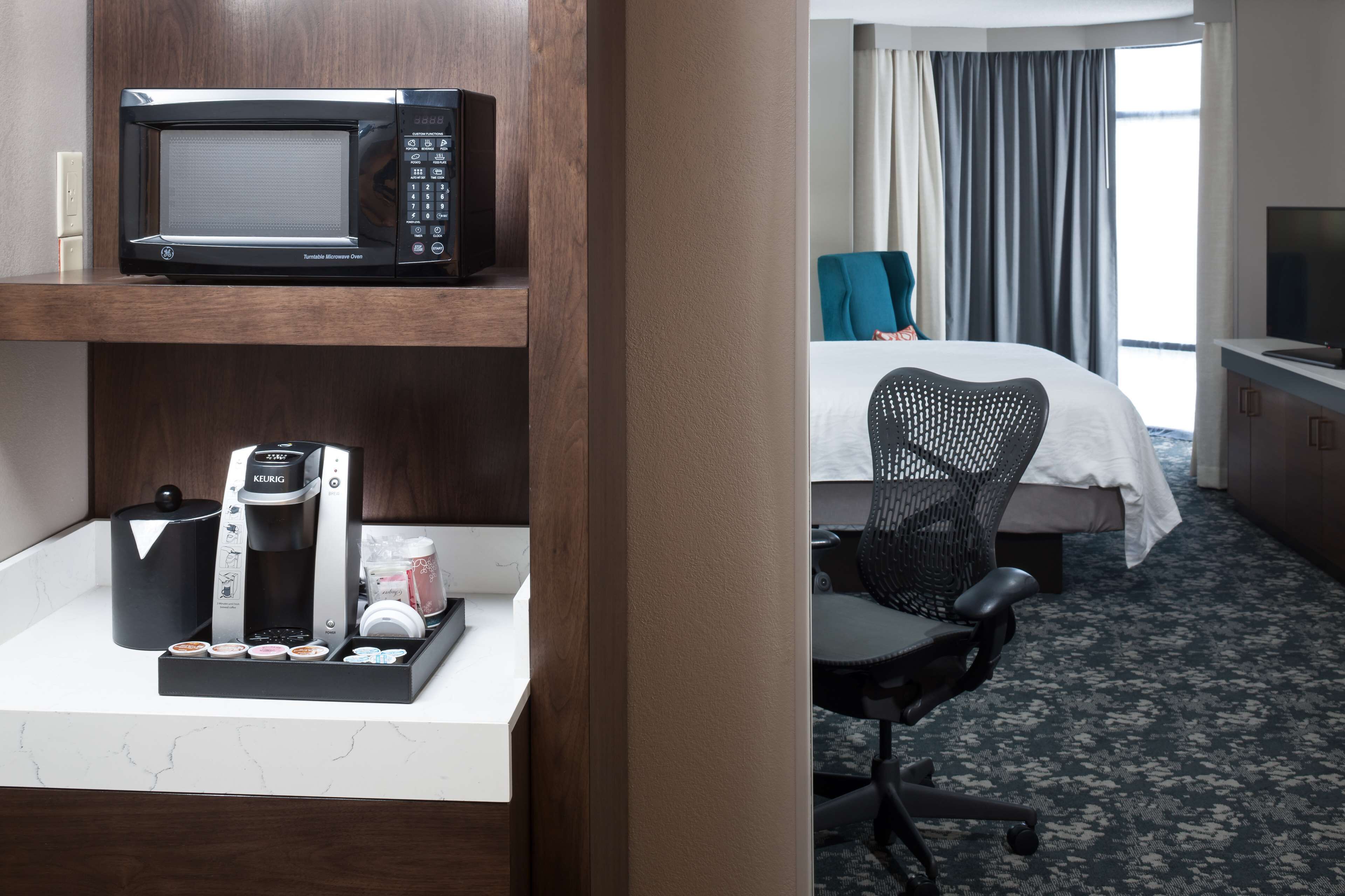 A hotel room with a microwave, coffee maker, and a bed with a view of the outdoors.