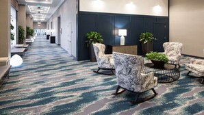 Een hotel lobby met een patroon vloerkleed, een zithoek met stoelen en een tafel, potplanten en een receptiebalie.