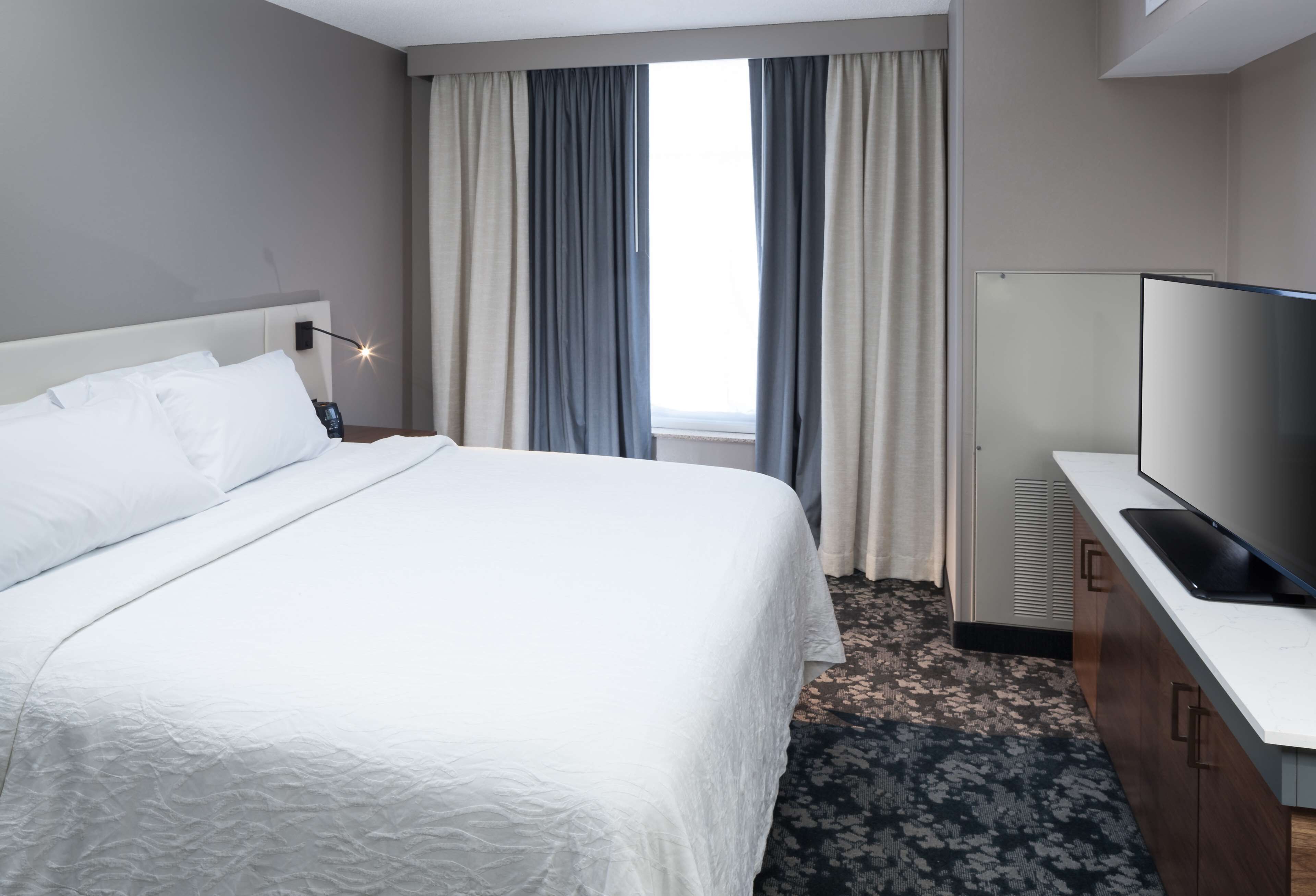 A hotel room with a large bed, a television, a desk, and a window with curtains.