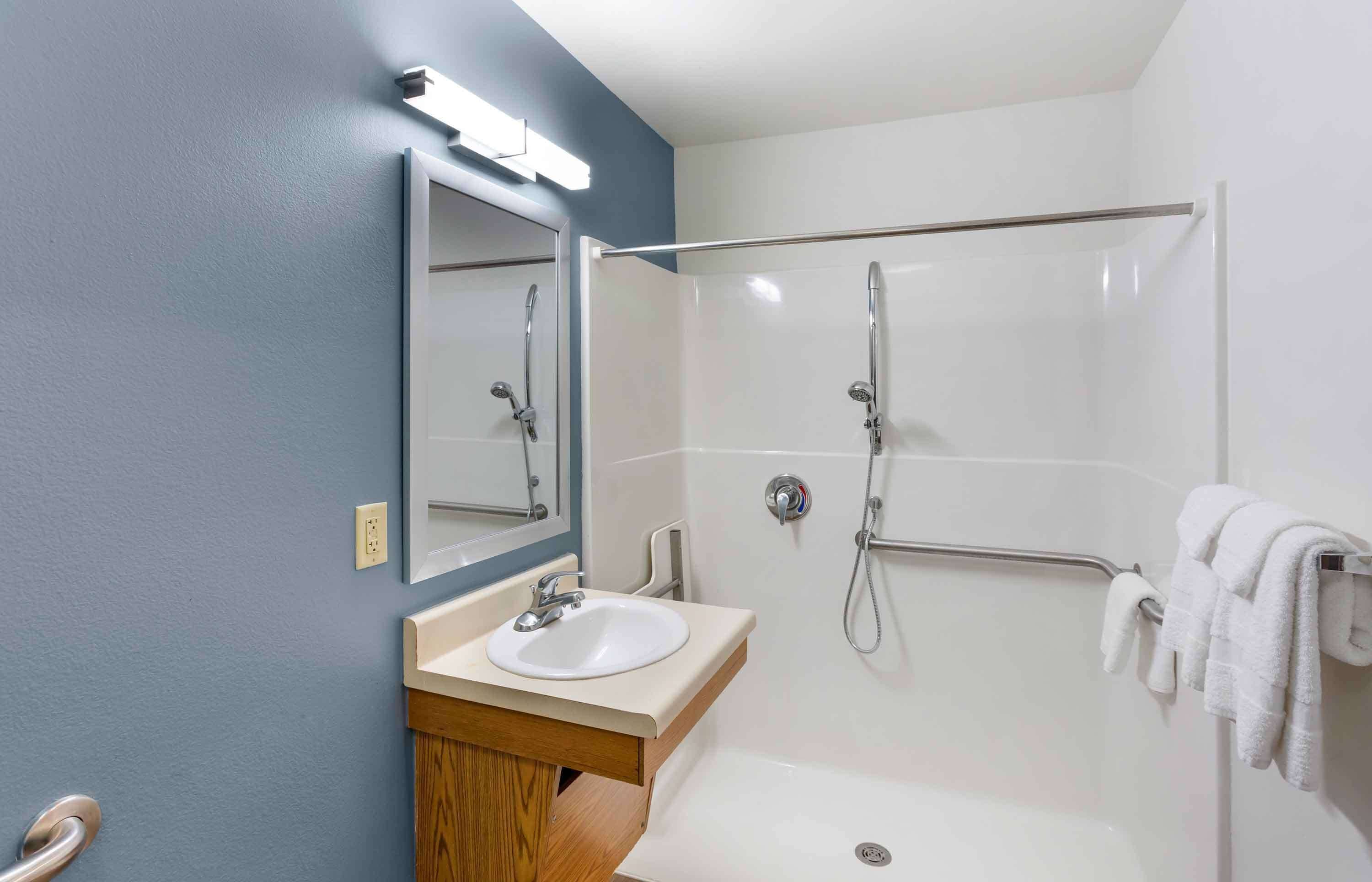 A bathroom with a sink, mirror, shower, and towel rack.