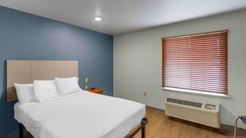 Une chambre à coucher comprenant un lit, une table de chevet, une fenêtre avec des stores et un appareil de climatisation.