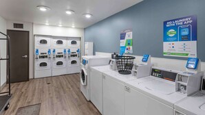 A modern laundry facility with multiple washing machines and dryers, a digital payment kiosk, and a promotional poster for a mobile app. - Extended Stay America Select Suites - Ogden (Ogden)