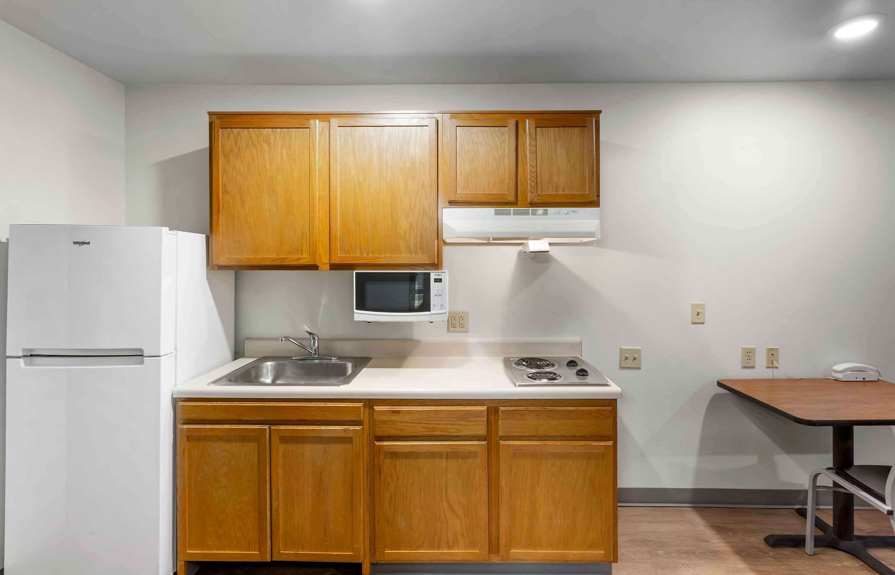 A compact kitchen with wooden cabinets, a white refrigerator, a microwave, a sink, and a small table.