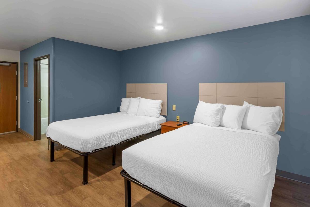 Habitación de hotel con dos camas individuales, piso de madera y pared azul.