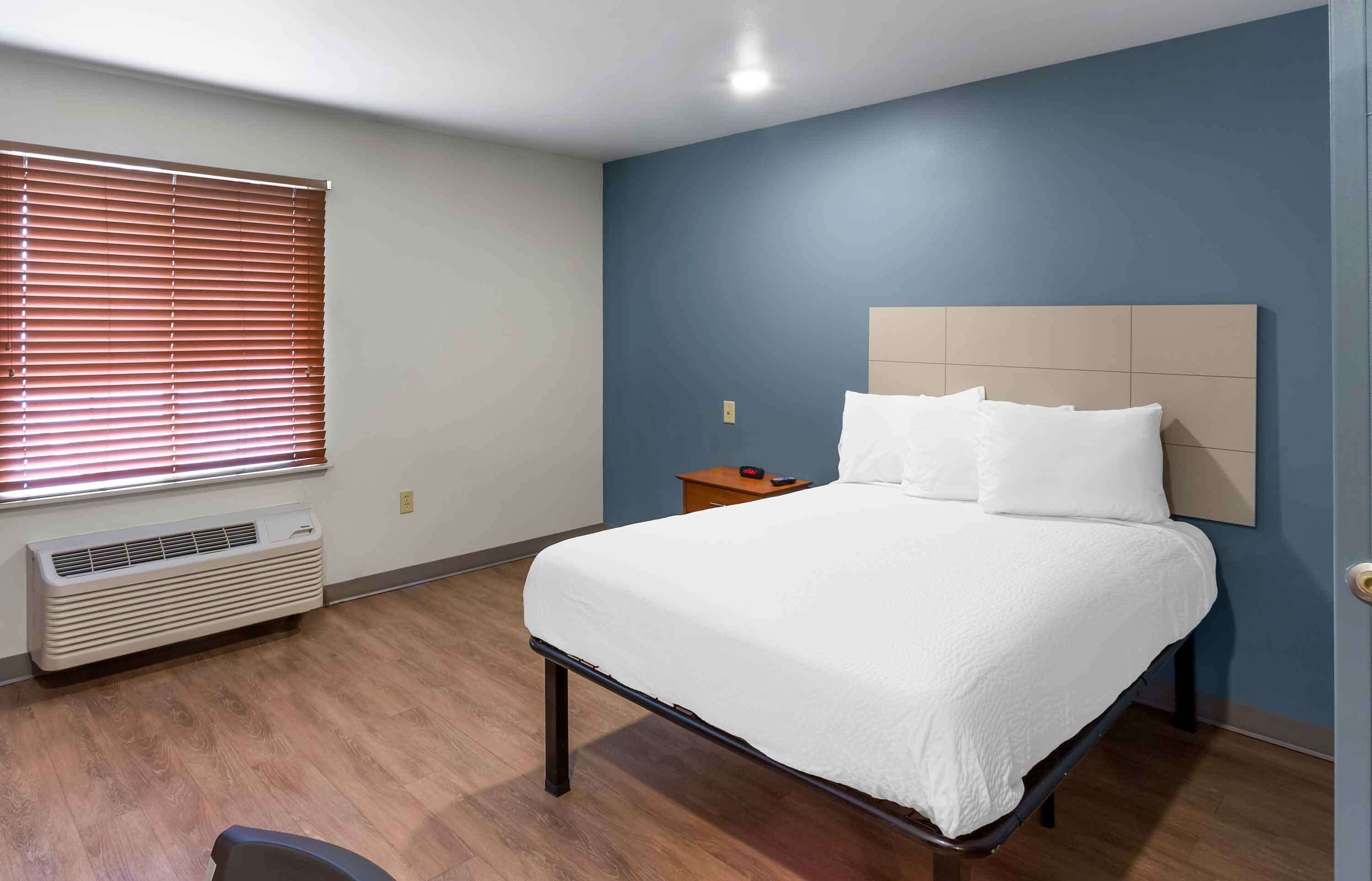 Une chambre à coucher comprenant un lit, une table de chevet, un radiateur et une fen être avec des stores.
