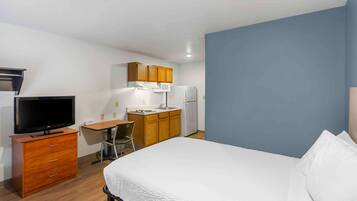 A compact hotel room with a bed, a desk, a television, and a kitchenette.