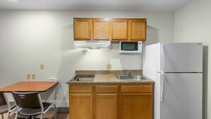 A small kitchen with wooden cabinets, a microwave, a refrigerator, a sink, and a table with chairs. - Extended Stay America Select Suites - Ogden (Ogden)