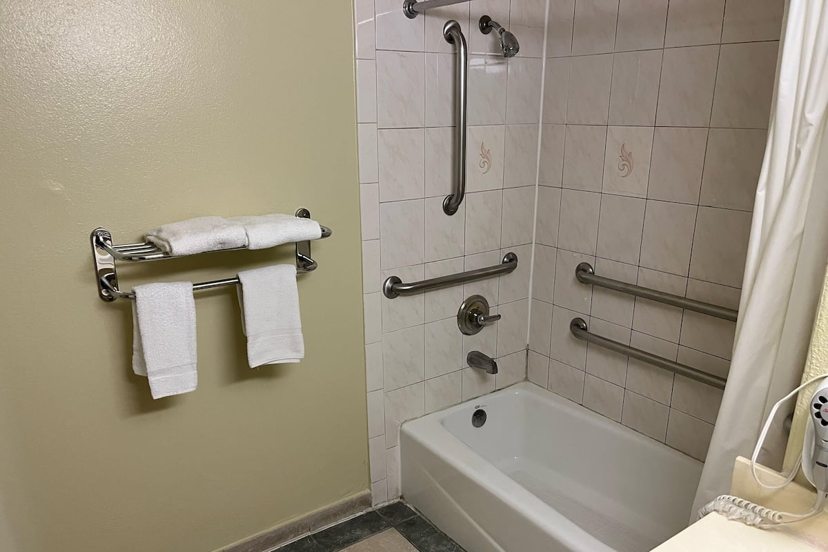 A bathroom with a bathtub, grab bars, a towel rack, and a showerhead.