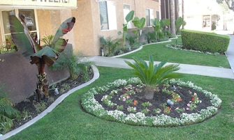 Un jardín bien cuidado con un parterre circular, un camino y un edificio con un letrero que dice 'Hotel'.