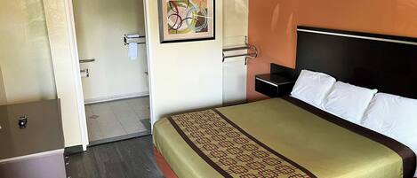 A hotel room with a bed, a nightstand, a framed abstract painting, a door, and a small desk.