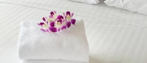 A neatly folded white towel with a purple flower on a bed.