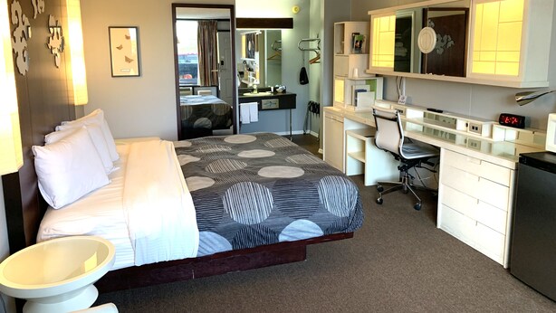 A hotel room with a bed, a desk, a chair, a mirror, a clock, and a bathroom. - Oxford Inn Ozark (Ozark)