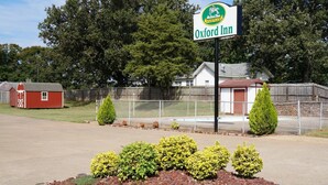 A sign for Oxford Inn, a fenced parking area, a red barn, and a white building with a red roof. - Oxford Inn Ozark (Ozark)