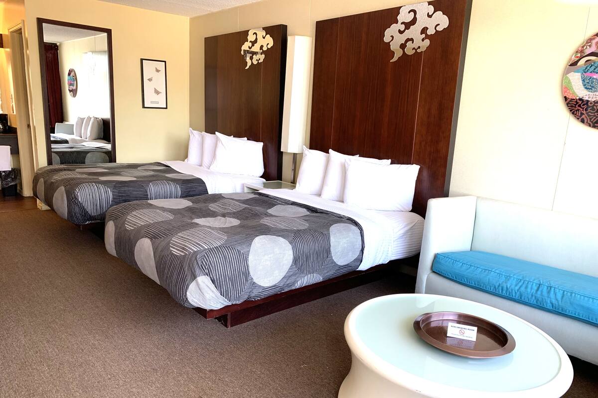 A hotel room with two beds, a sofa, a coffee table, and a smoking area sign.