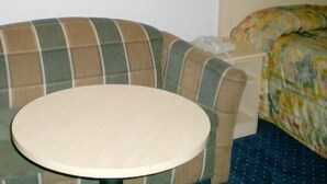 Een kamer met een ronde tafel, een geruit fauteuil, een bed met een bloemenbedekking en een klein nachtkastje met een telefoon.