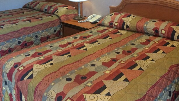 Een hotelkamer met twee bedden, elk met een gebloemd quilt, een bedlamp en een lijst met een foto aan de muur.