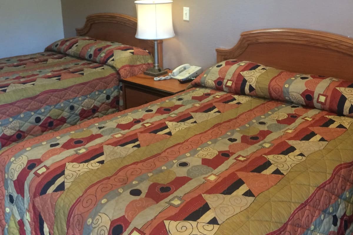 Een hotelkamer met twee bedden, elk met een gebloemd quilt, een bedlamp en een lijst met een foto aan de muur.