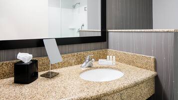 A bathroom with a granite countertop, a white sink, a mirror, and a towel dispenser.
