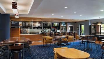 Un restaurante moderno con mesas y sillas de madera, una zona de bar y una barra con mostradores de menú.