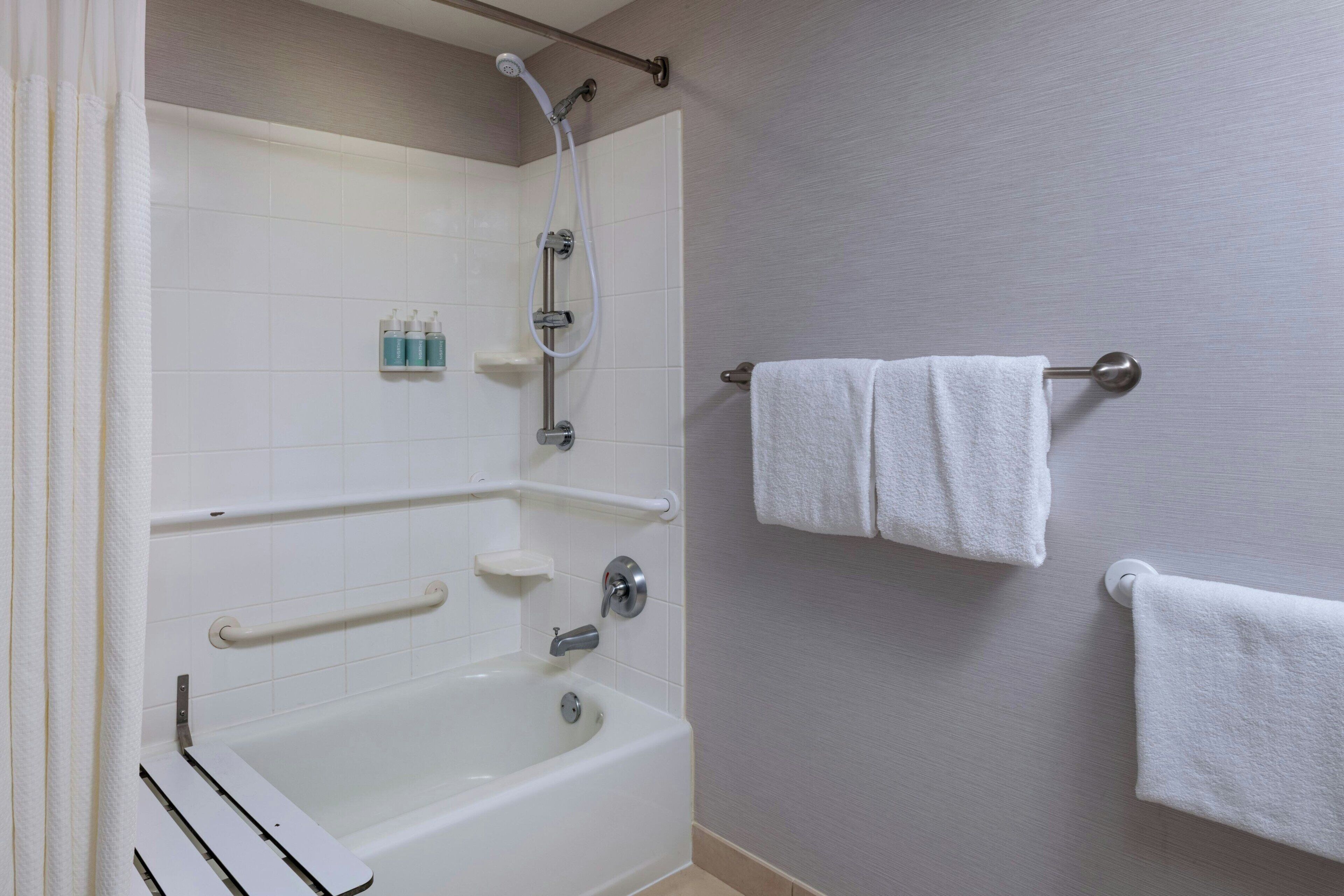 A bathroom with a bathtub, grab bars, a towel rack, and a showerhead.