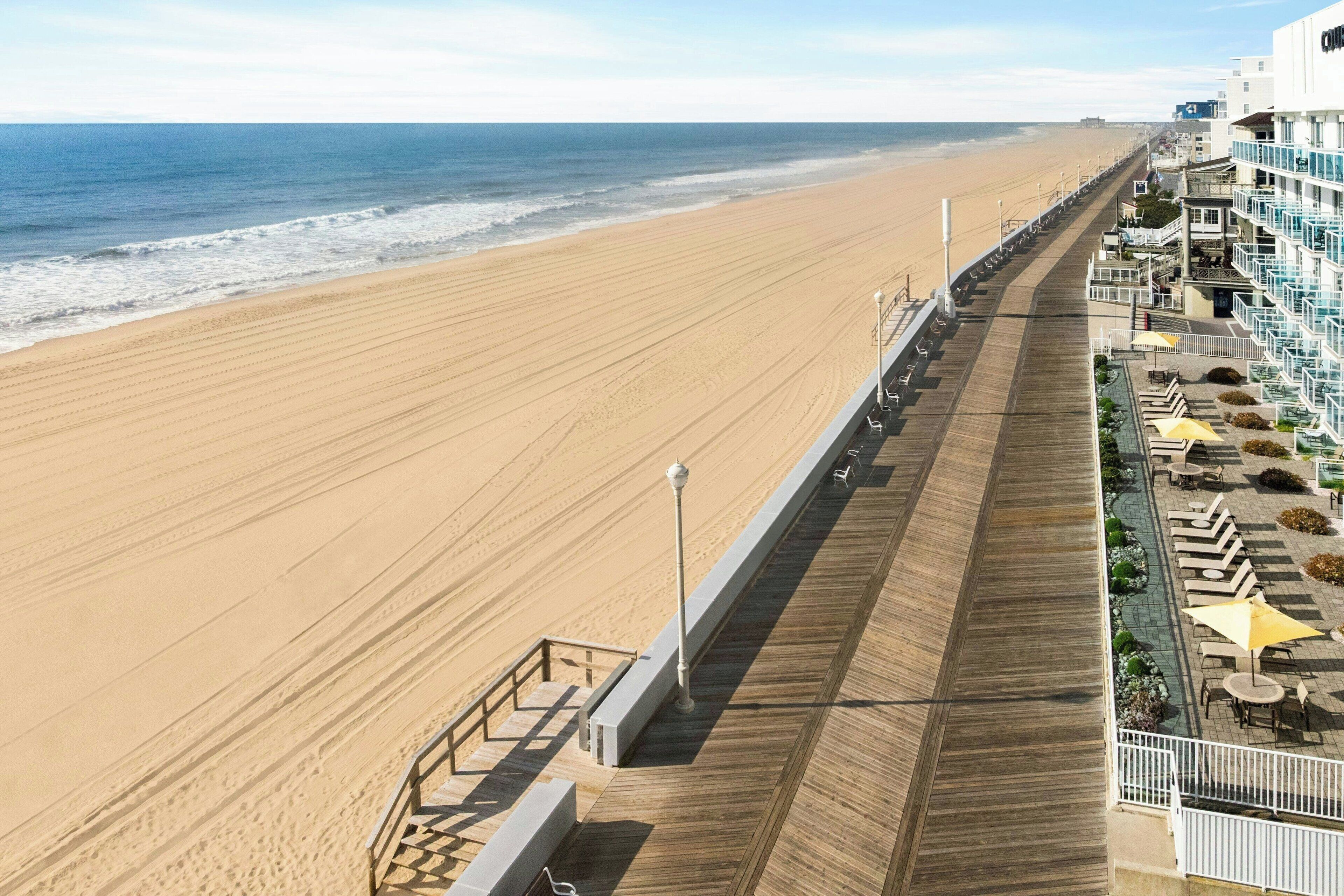 Un hotel frente al mar con un paseo marítimo de madera, mobiliario exterior y vistas al océano.