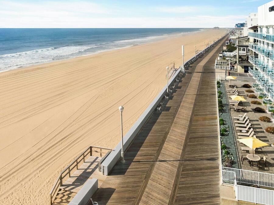Un hotel frente al mar con un paseo marítimo de madera, mobiliario exterior y vistas al océano.