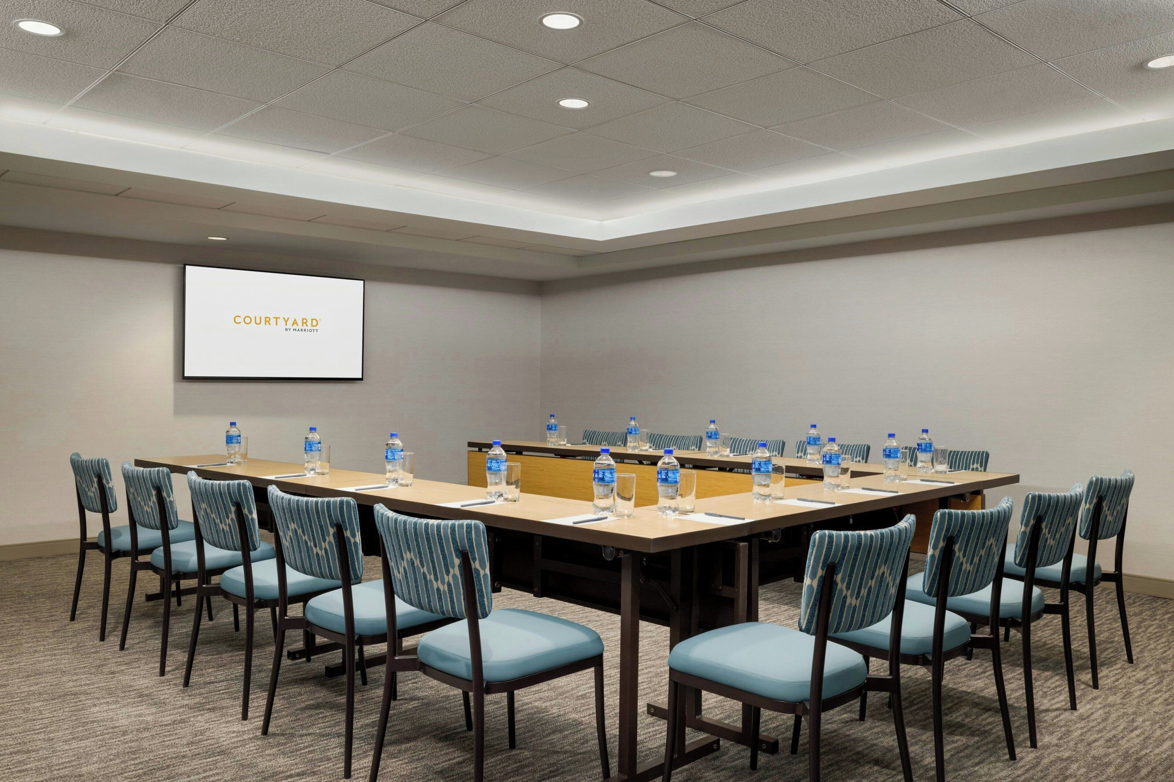 A conference room with a long table, chairs, water bottles, and a screen displaying "COURTYARD".