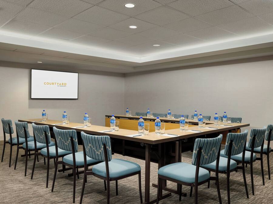 A conference room with a long table, chairs, water bottles, and a screen displaying "COURTYARD".