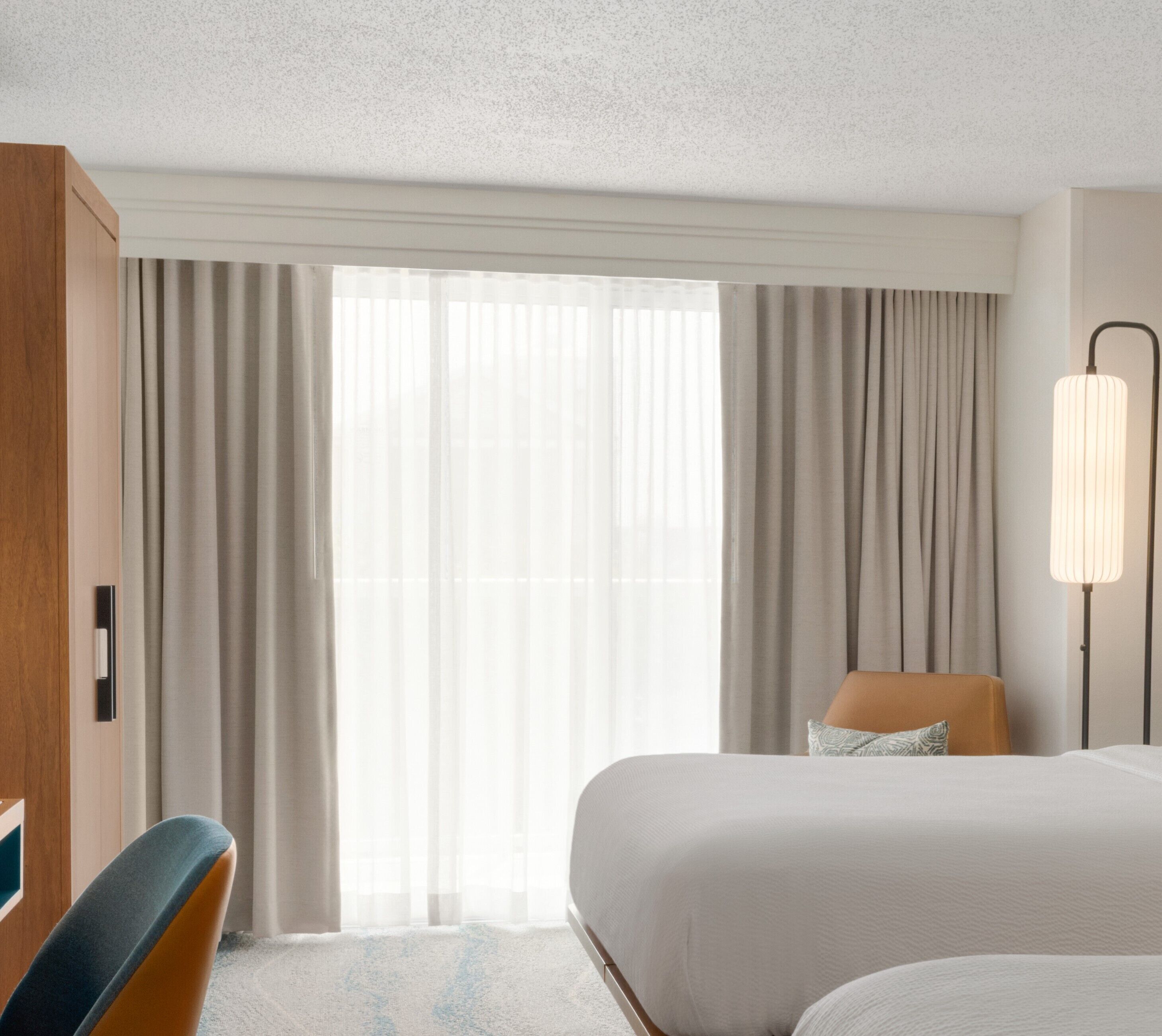 A hotel room with a bed, a chair, a desk, and a lamp.