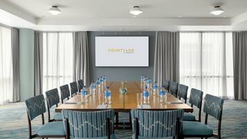 Une salle de conférence avec une longue table, des chaises, un écran affichant le logo « COURTYARD BY MARRIOTT » et des bouteilles d’eau.
